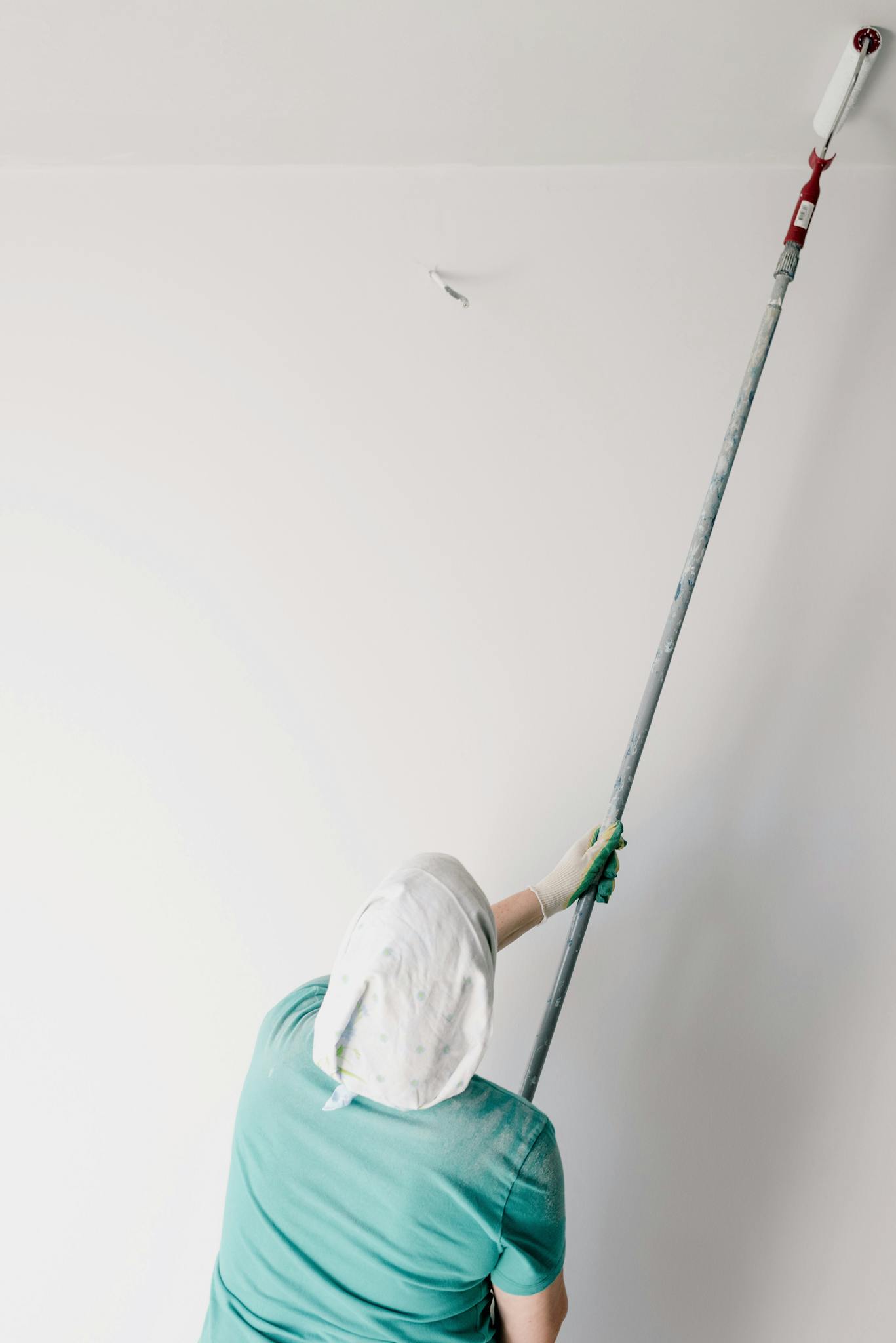 Back view of anonymous male worker with roller painting ceiling while working at home